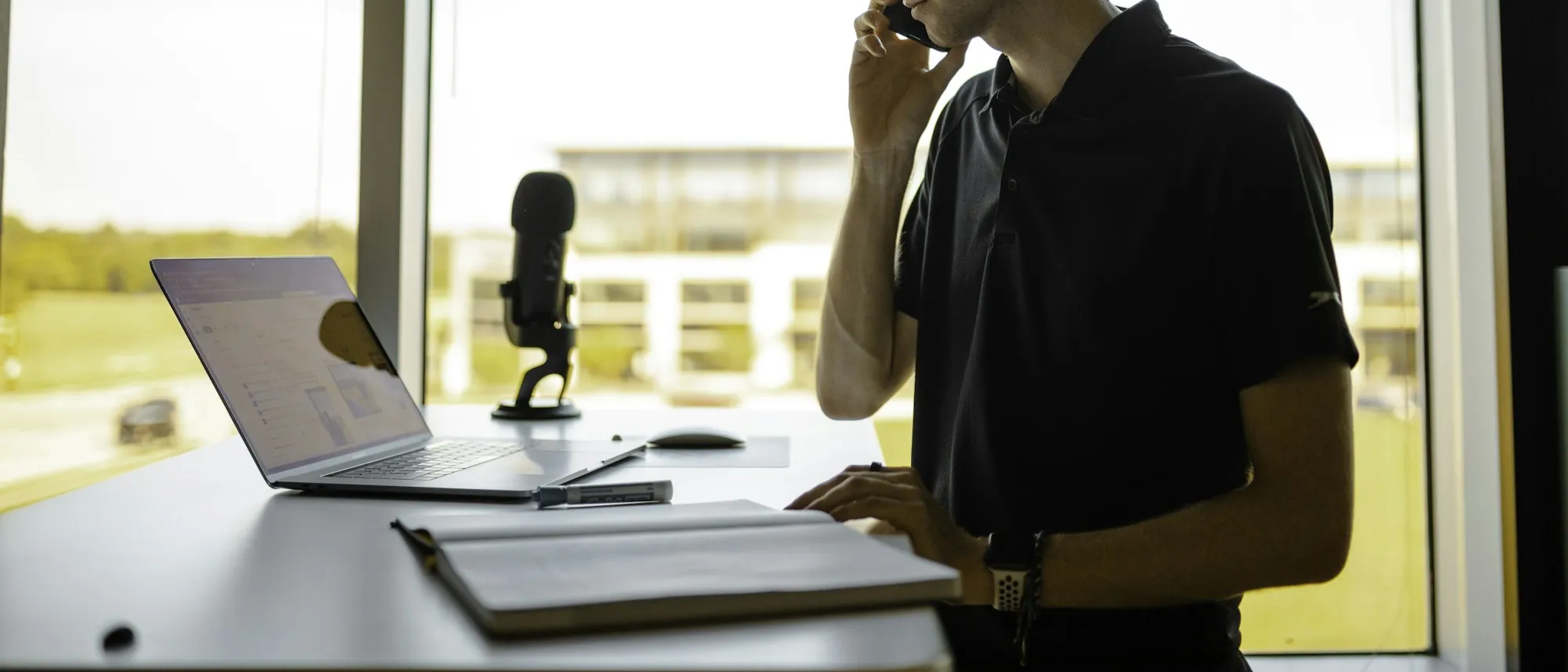A self-employed man on a phone call at his desk, late afternoon light through the window
