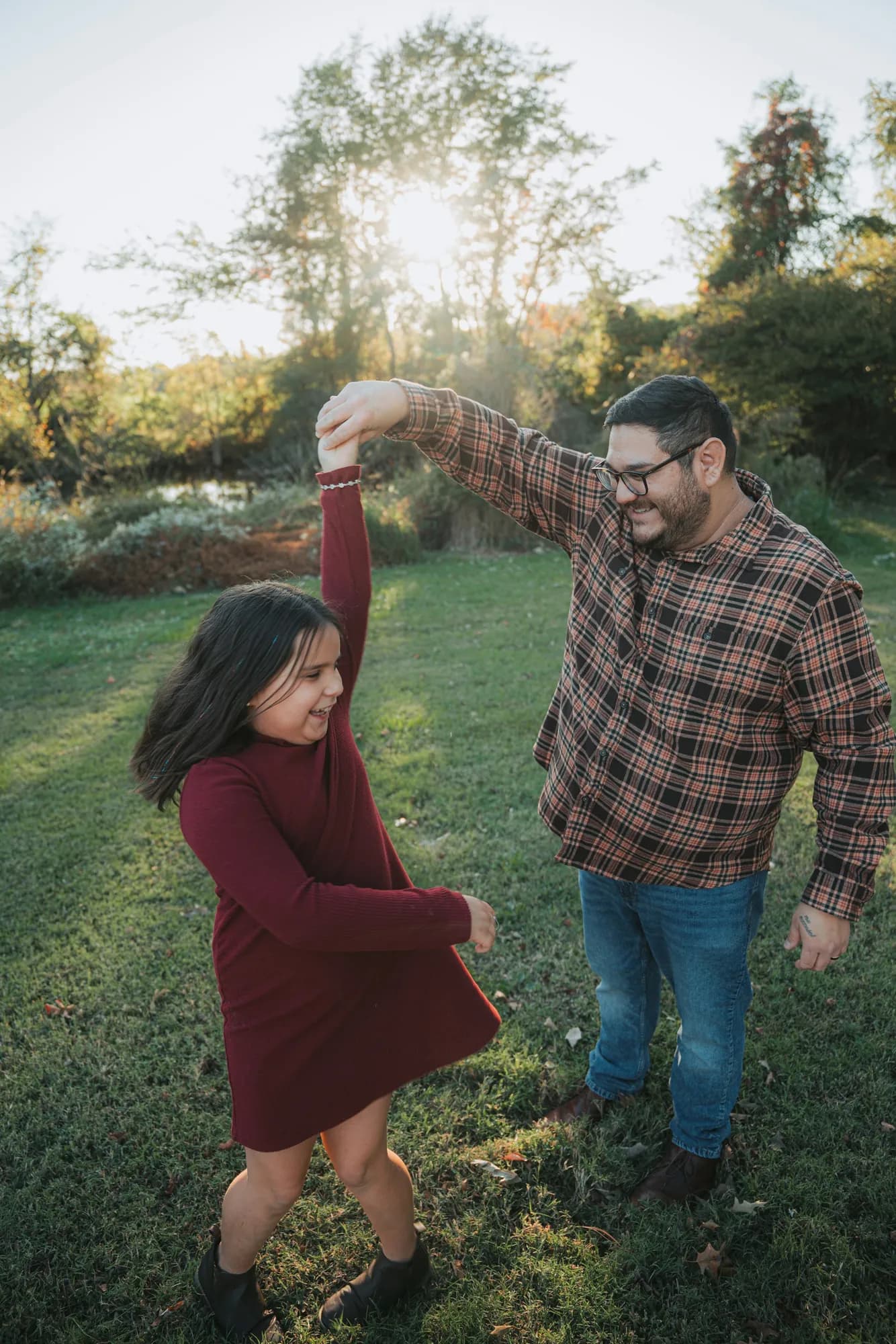 A father and daughter dancing together in a park at golden hour