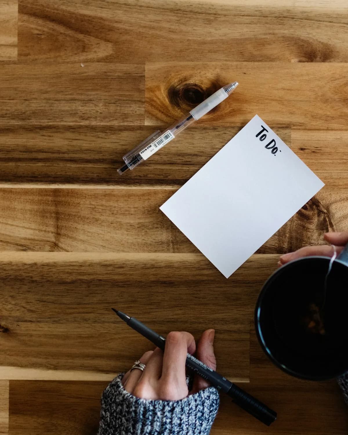 A wooden kitchen table from above: a blank sheet of paper, a pen, and a cup of coffee